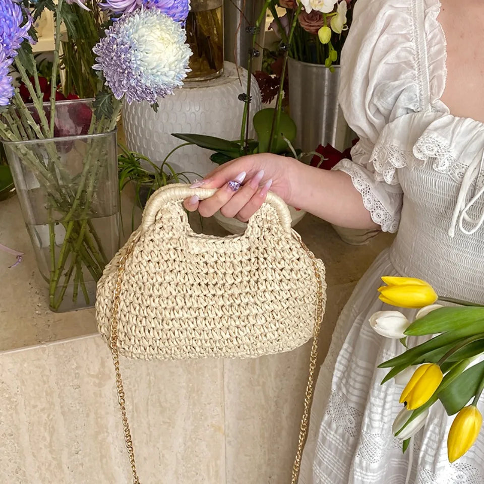 Person holding a woven handbag with flowers and a dress in the background