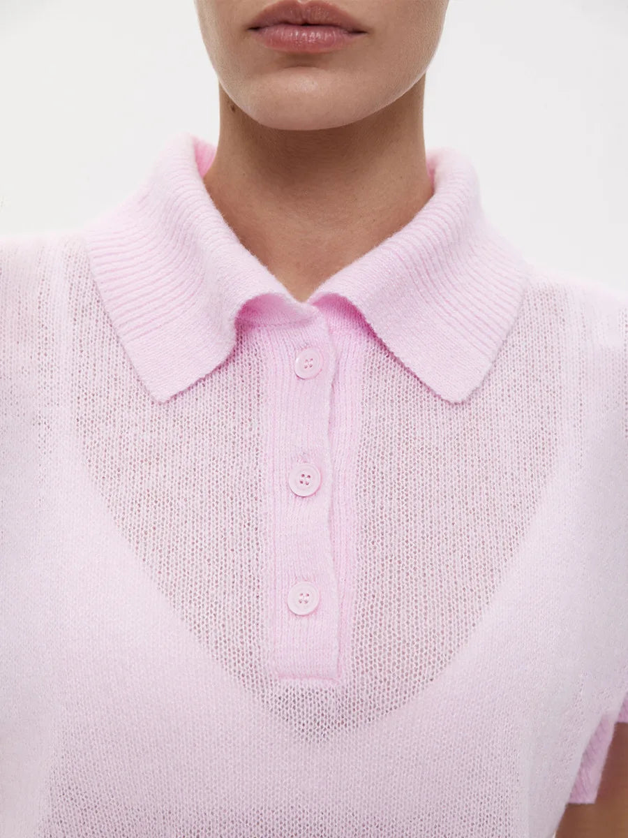 Close-up of a person wearing a light pink knitted polo shirt with a plain background