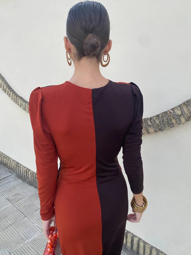Person wearing a two-tone dress with red and black sections, standing against a white wall.