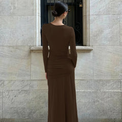 Woman in a brown dress standing against a stone wall.