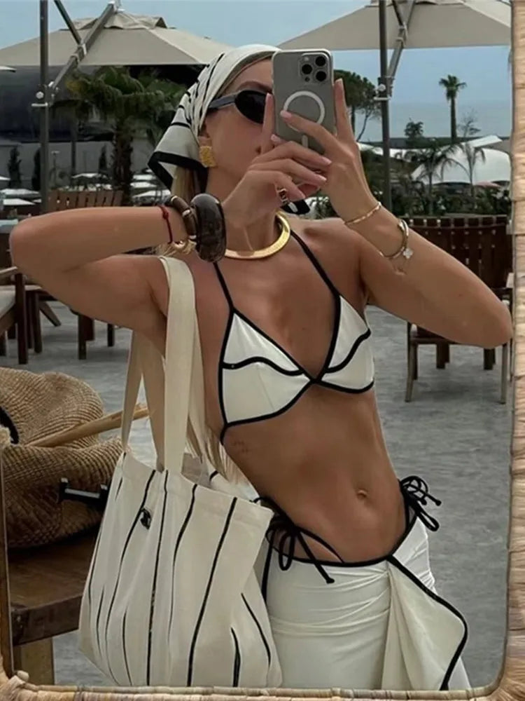 Model wearing a white bikini and ruffled skirt with contrast trim.