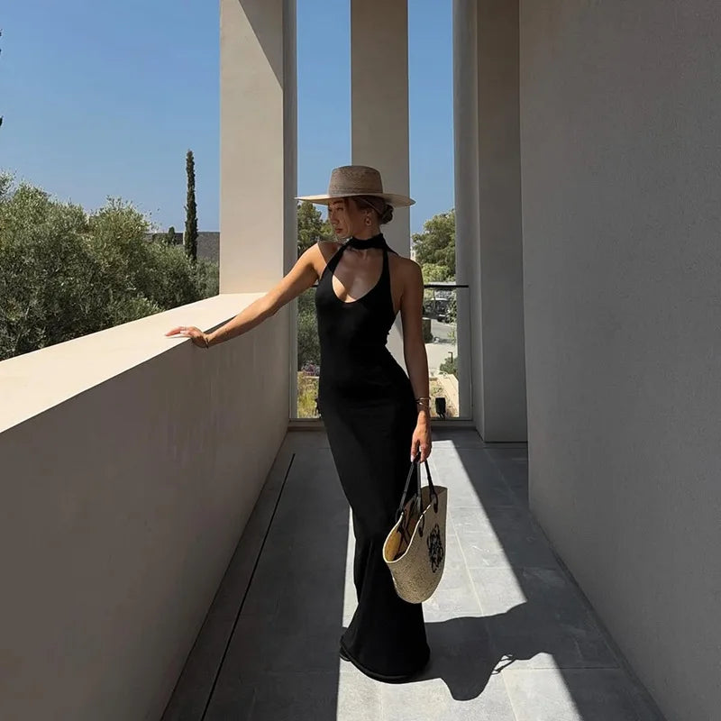 Woman in a black dress and straw hat standing on a balcony with a scenic view.