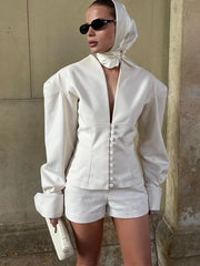 Person wearing a white outfit with a headscarf against a beige wall.