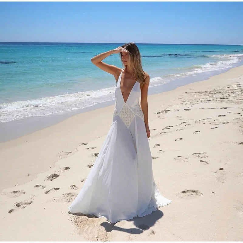 Woman in a white dress standing on a sandy beach with clear blue water and sky.