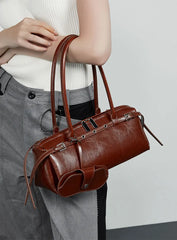 Brown leather handbag held by a person wearing gray pants against a light background