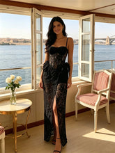 Black lace corset gown with spaghetti straps and a side split, modeled by a woman standing by a window.