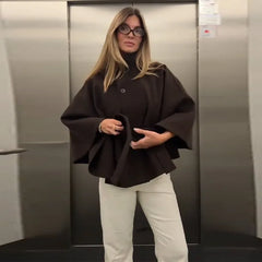Woman wearing a black cape and white pants standing in an elevator.