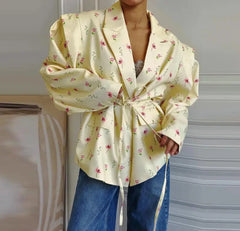 Person wearing a light yellow floral blouse with a tie front, standing against a neutral background.