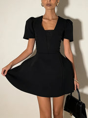 Woman wearing a black dress holding a black handbag against a neutral background