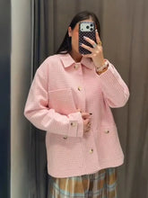 Person wearing a pink checkered shirt taking a mirror selfie.