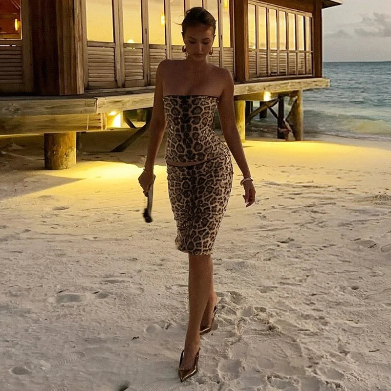 Woman in a leopard print dress walking on a sandy beach with ocean view.