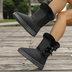 Black winter boots with fur trim worn by a person on a wooden floor.