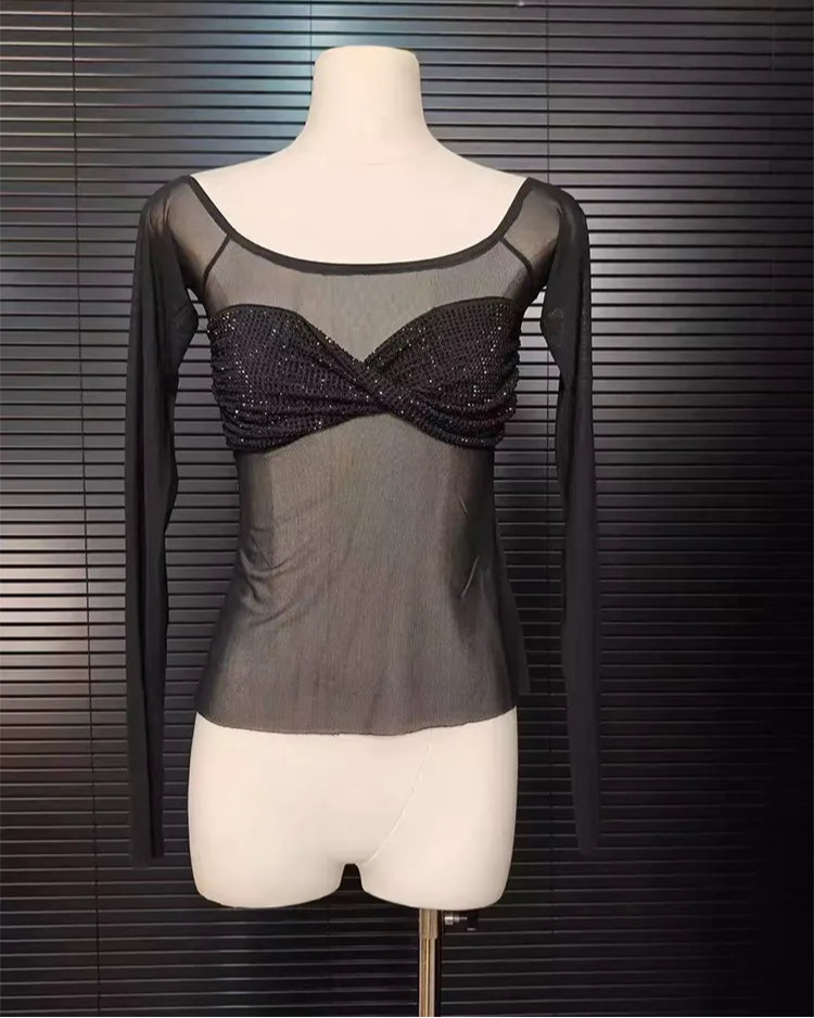 Mannequin wearing a black long-sleeve top with sheer overlay and beaded details against a dark background.