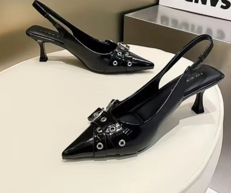 Black high-heeled shoes with decorative elements on a white platform.