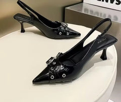 Black high-heeled shoes with decorative elements on a white platform.