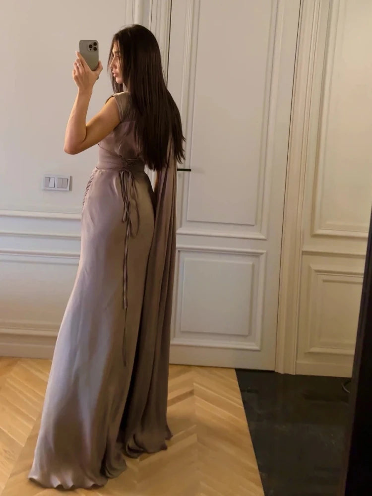 Woman taking a mirror selfie wearing a long, flowing dress in a room with white paneled walls.