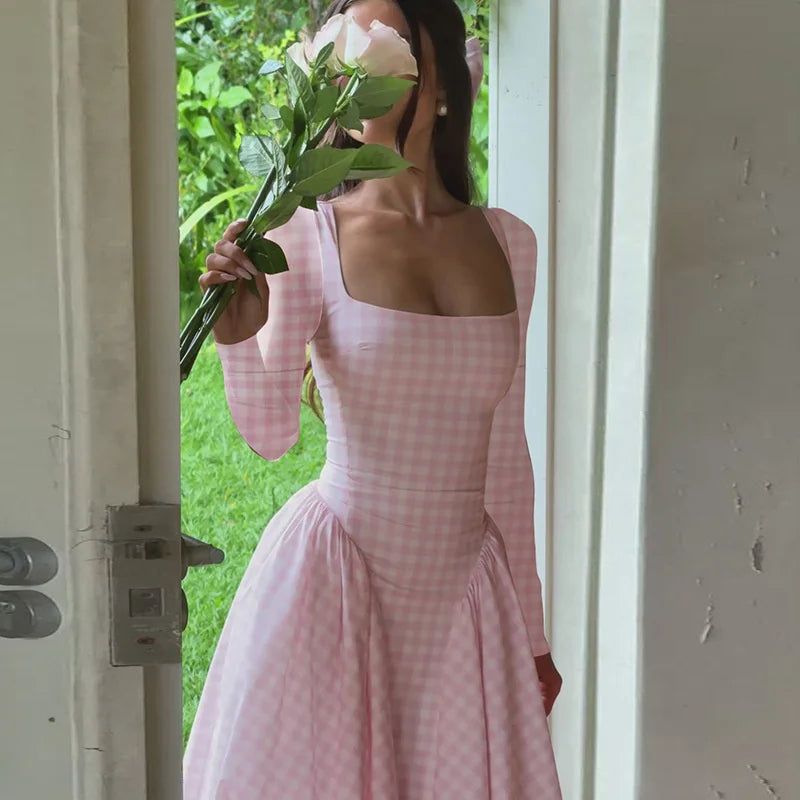 Woman in a pink checkered dress holding flowers, standing in a doorway.