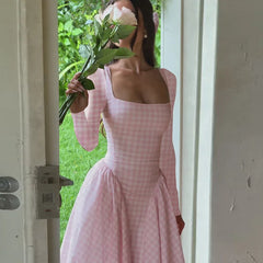 Woman in a pink checkered dress holding flowers, standing in a doorway.