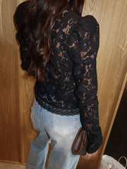 Person wearing a black lace top and light blue jeans against a wooden wall.