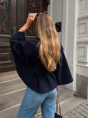 Person wearing a black jacket and blue jeans standing in front of a building entrance.