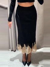 Person wearing a black skirt with lace hem and black high-heeled shoes against a neutral background