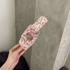 Floral-patterned sandal held by a hand against a neutral background