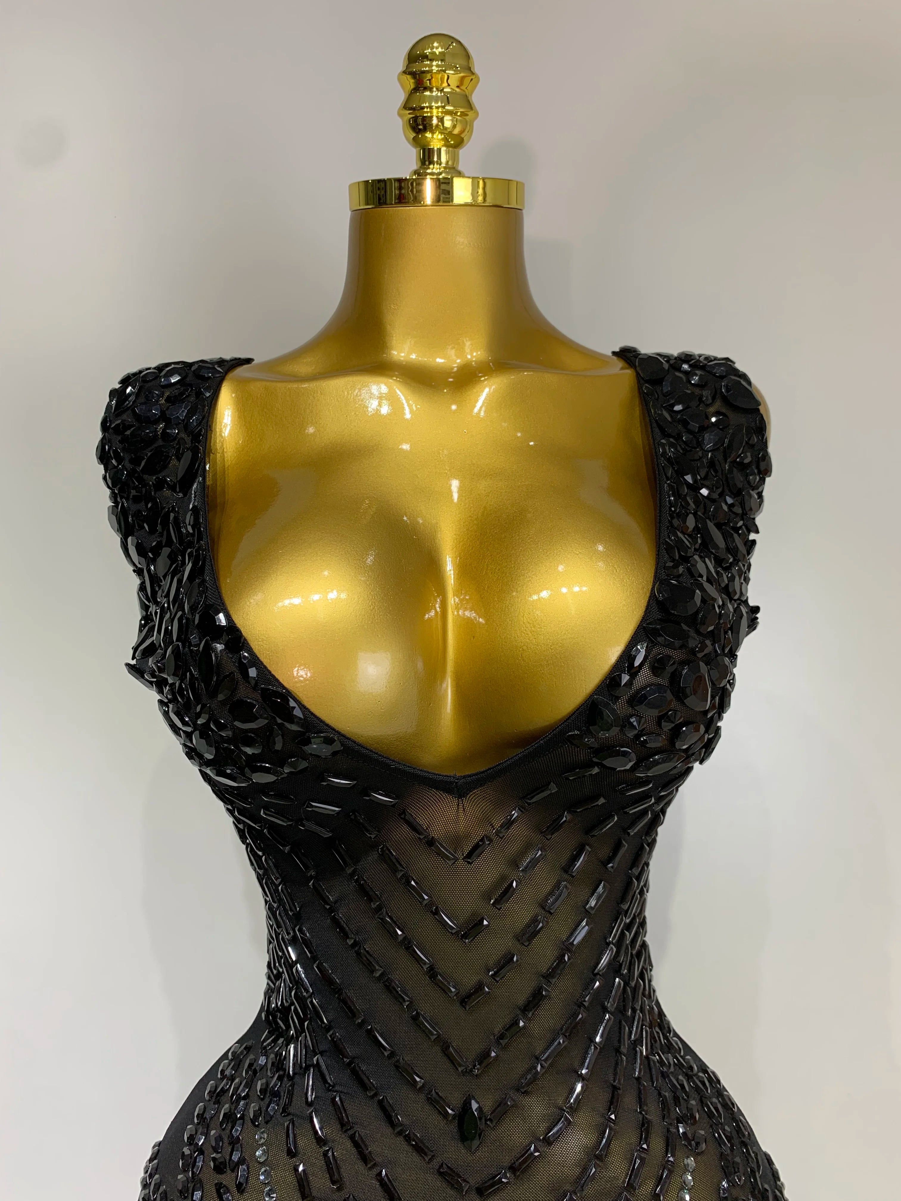 Mannequin wearing a black beaded dress with a gold top on a white background