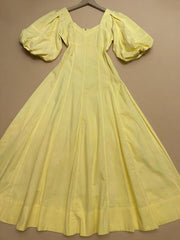 Yellow dress with puffed sleeves on a hanger against a brown background