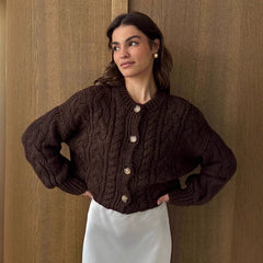 Woman wearing a brown cable knit cardigan against a wooden paneled wall.