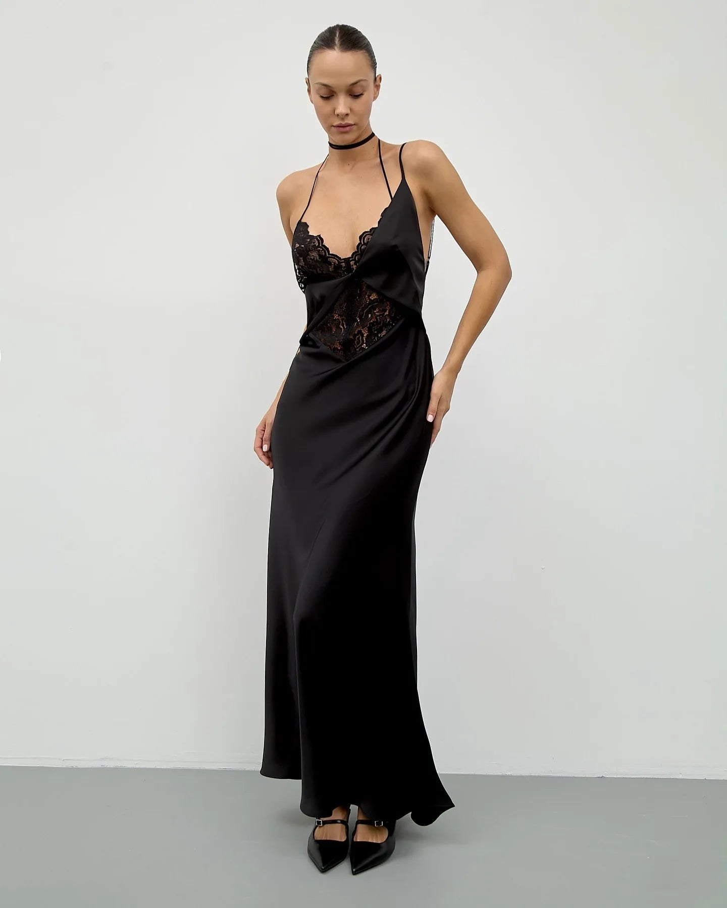 Woman wearing a black satin evening gown with lace details against a white background