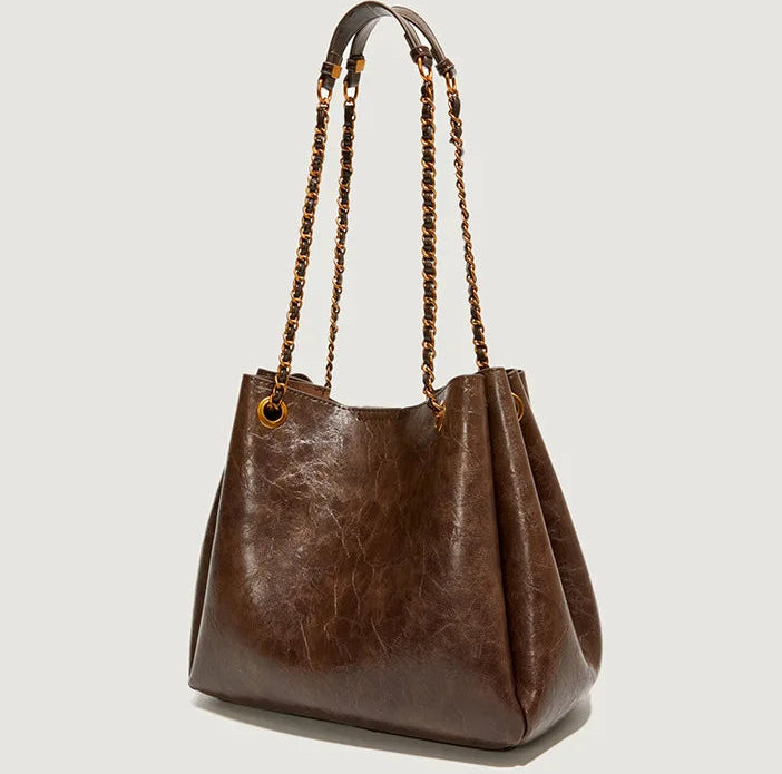 Brown leather handbag with chain handles on a light gray background