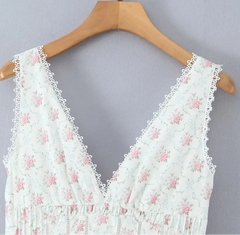 White lace top with pink floral patterns on a wooden hanger against a gray background