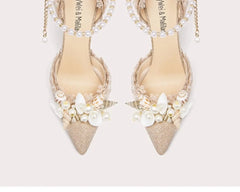 Pair of beige pointed-toe shoes with pearl embellishments on a light background