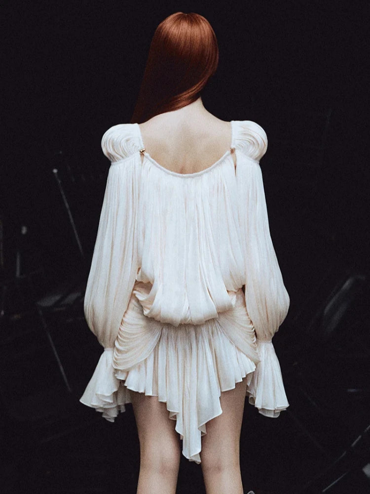 Person wearing a white dress with puffed sleeves and a high-low hemline on a dark background
