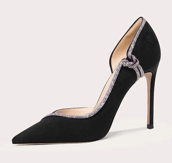 Black high-heeled shoe with decorative strap on a light gray background