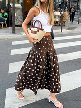 Woman in a white top and brown polka dot skirt crossing a street.