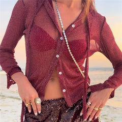 Person wearing a sheer red cardigan over a black outfit on a beach.