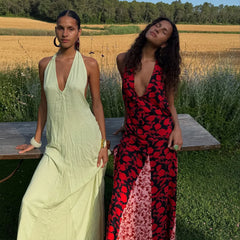 Two women in dresses sitting on a bench in a field.