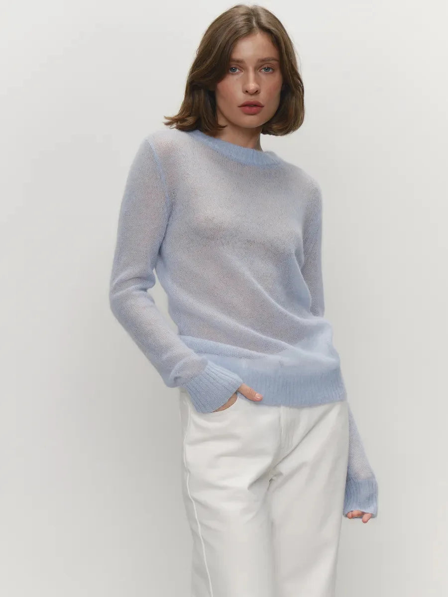 Woman wearing a light blue sweater and white pants on a plain background