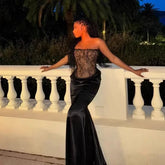 Woman in a black evening gown standing on a white railing with a nighttime outdoor setting.