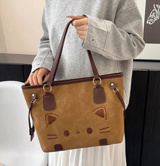 Person holding a brown suede-like tote bag with a cat face design