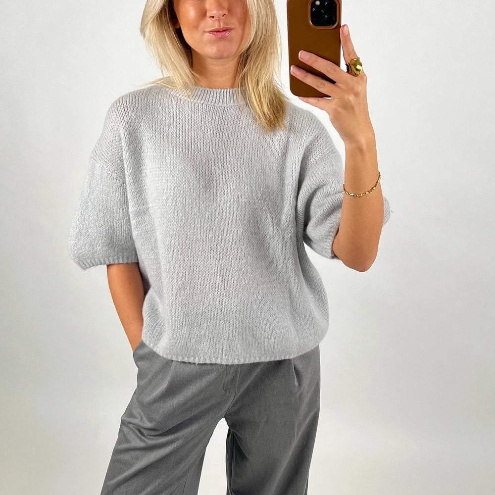 Person wearing a gray sweater and pants against a plain background