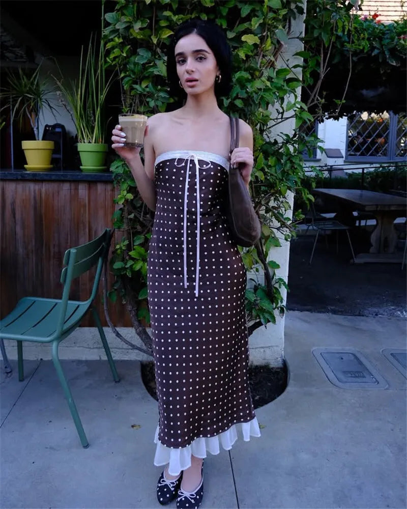 Woman in a brown and white polka dot dress holding a cup outdoors.