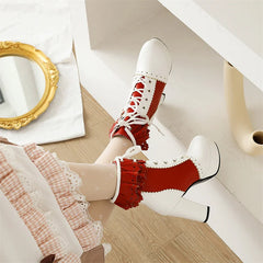 White high-heeled shoes with red lace details worn by a person sitting on a couch.