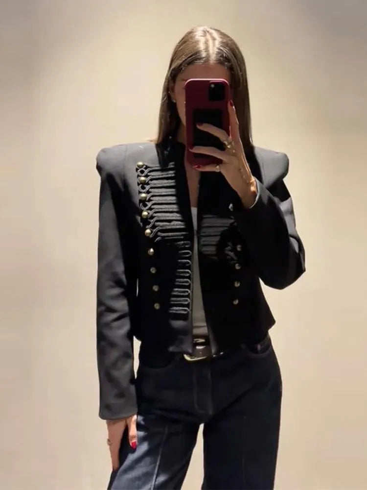Woman wearing a black cropped military style jacket with gold buttons and cord braiding