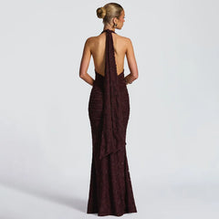 Woman wearing a burgundy evening gown with a halter neck and open back on a light gray background