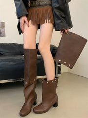 Person wearing brown knee-high boots and holding a matching bag indoors.