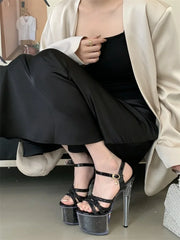 Person wearing black high-heeled sandals with clear platforms, sitting on a chair.