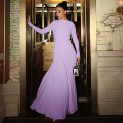 Woman in a long purple dress standing in an elegant interior setting.