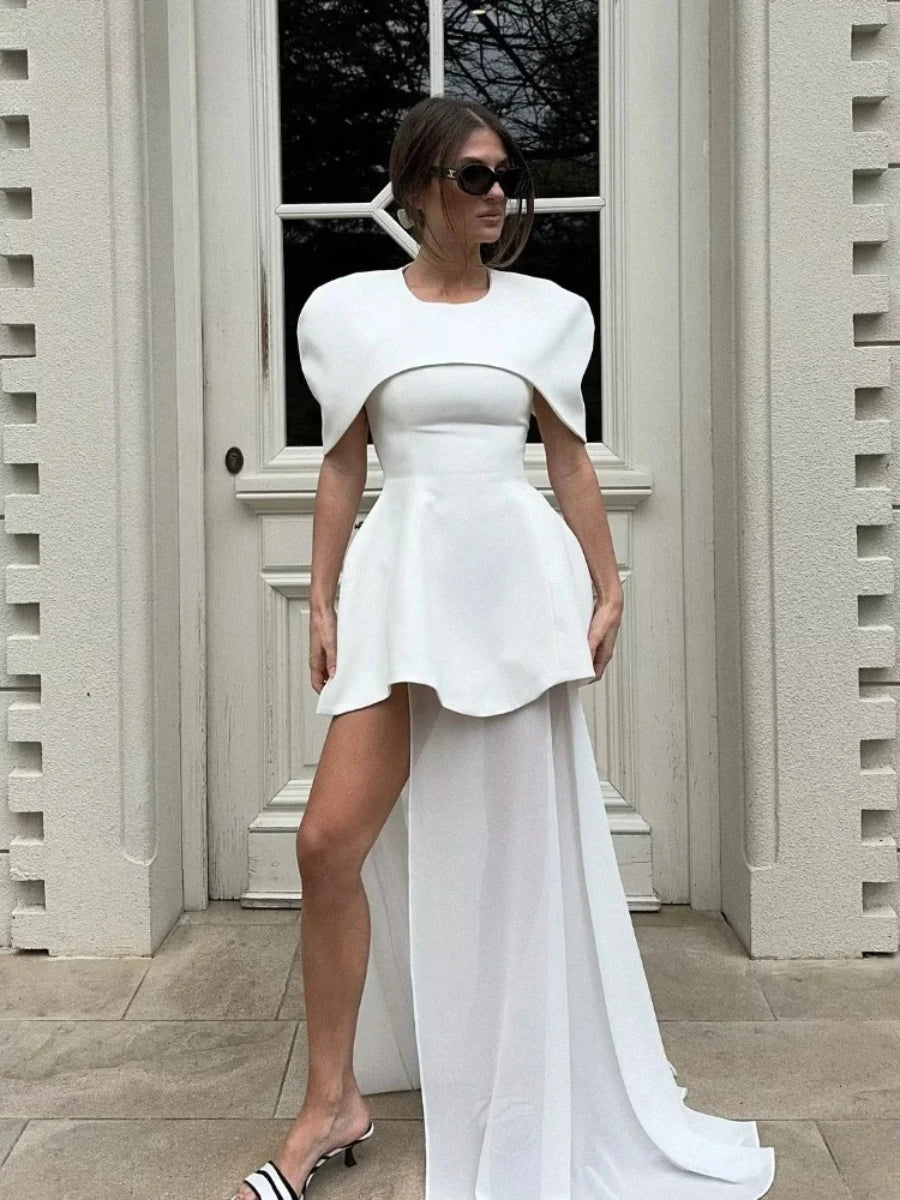 Woman wearing a white dress with a high-low hem in front of a building.